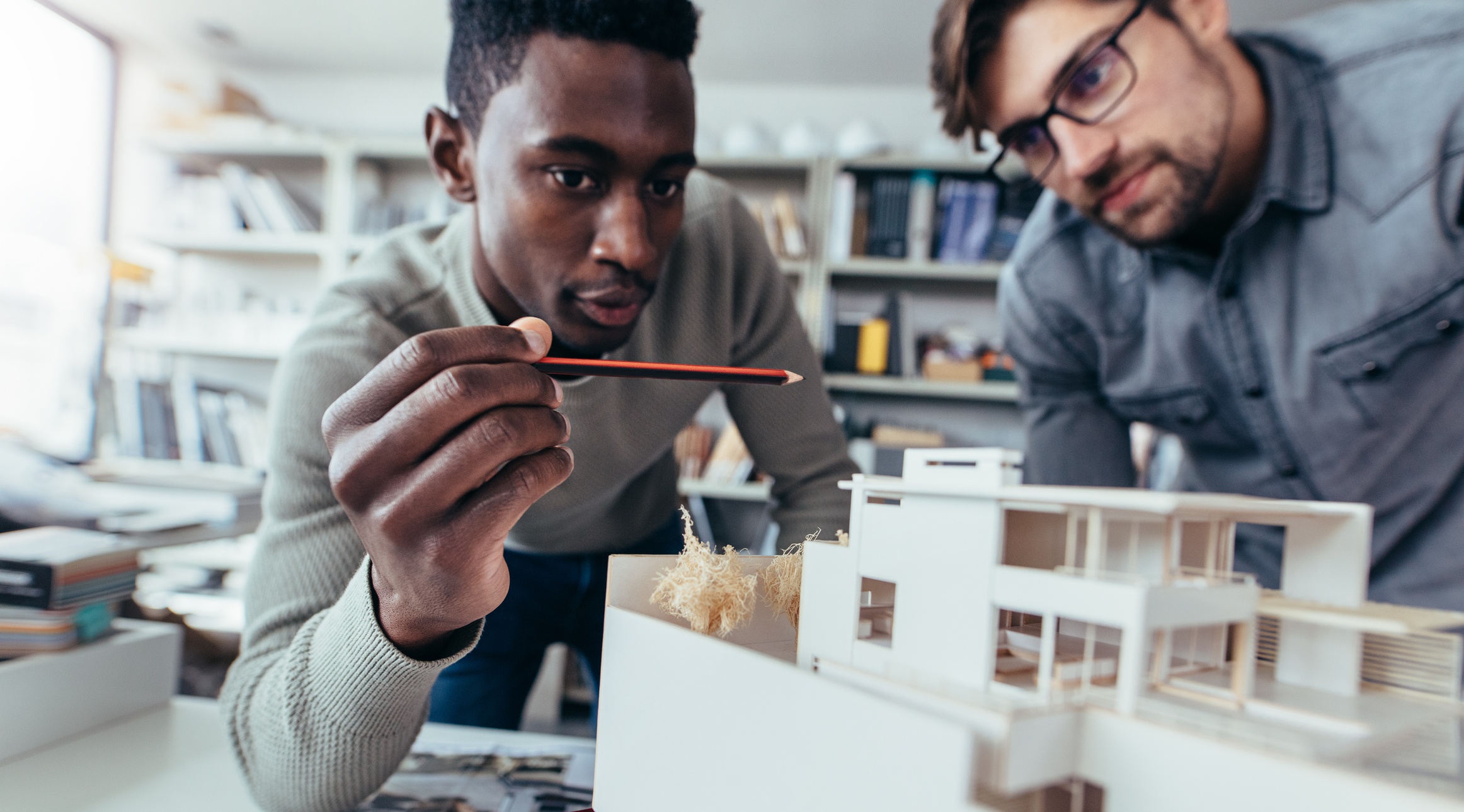 Two male architects in office discussing construction project. Young men working together on new building model.